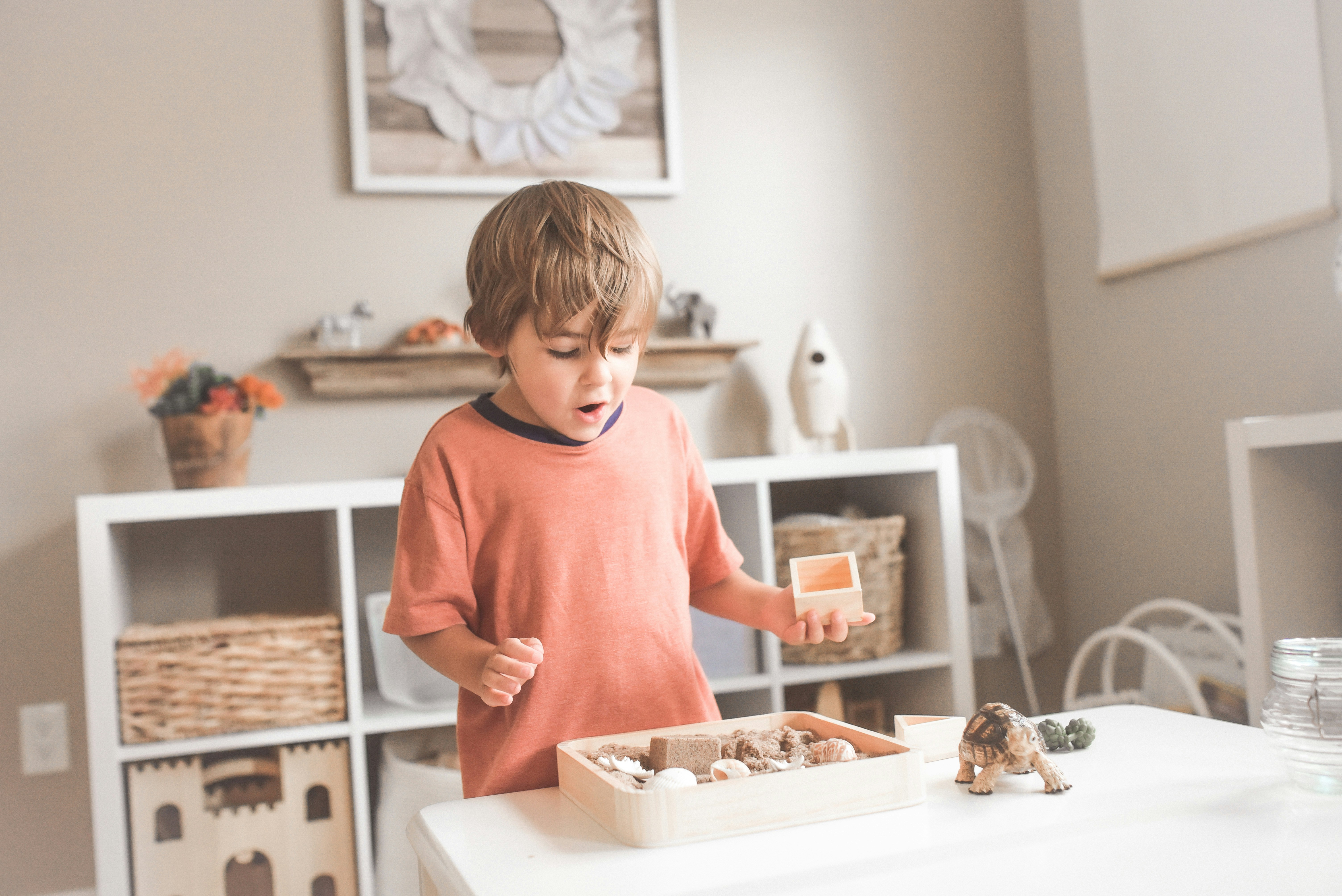 A child exploring a sensory play tray in a tidy, organized play space with cube shelving