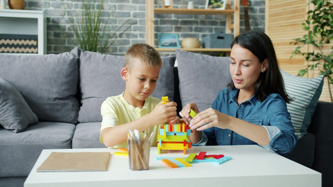A specialist guiding a young boy as he builds a colorful stacking-block tower at a table