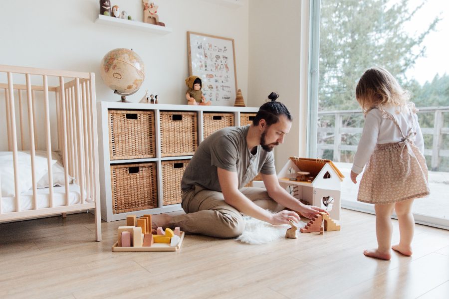 A father and daughter tidying wooden toys into baskets in a calm, organized nursery